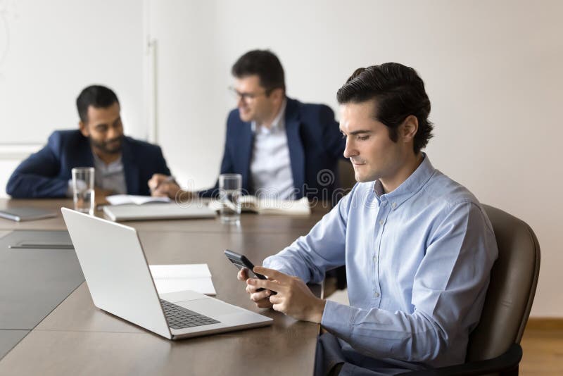 Young focused businessman using smartphone sit at desk with laptop royalty free stock photos