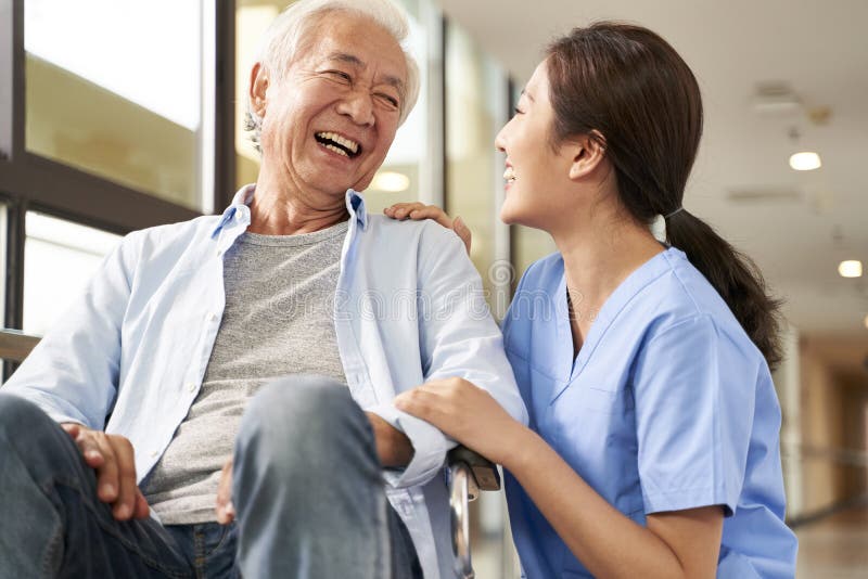 Young friendly asian female caregiver talking to elderly man in nursing home