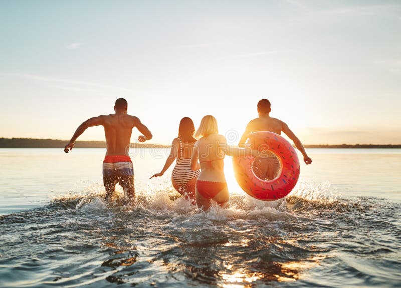 Laughing friends splashing each other in a lake at sunset