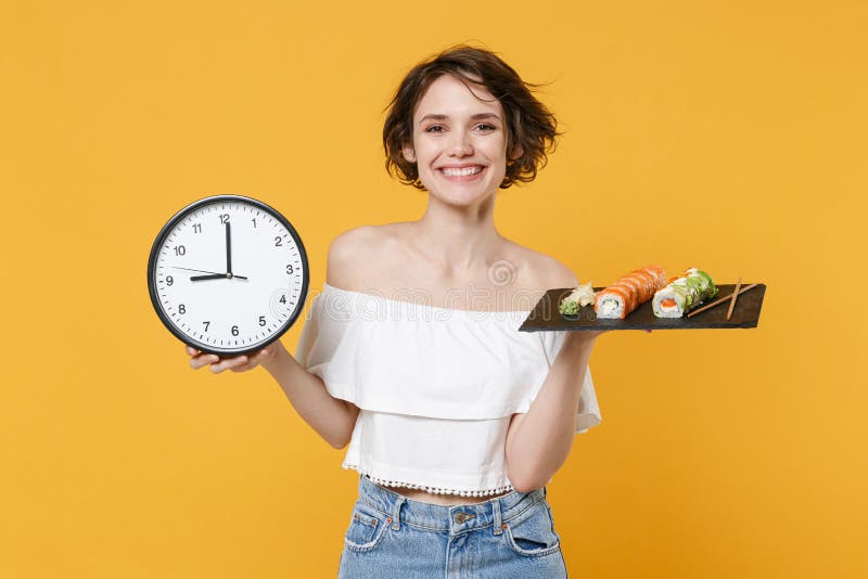 Young fun woman girl in casual clothes hold in hand clock makizushi sushi roll served on black plate traditional stock photo