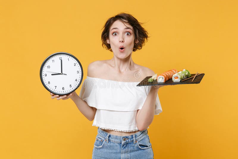 Young fun woman girl in casual clothes hold in hand clock makizushi sushi roll served on black plate traditional stock photography