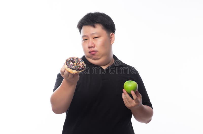 Young Funny Fat Asian man choosing between chocolate donuts and green apple isolated on white background