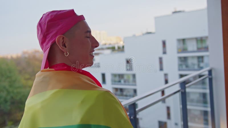 Young gay man with rainbow flag on the balcony turning around with a big smile