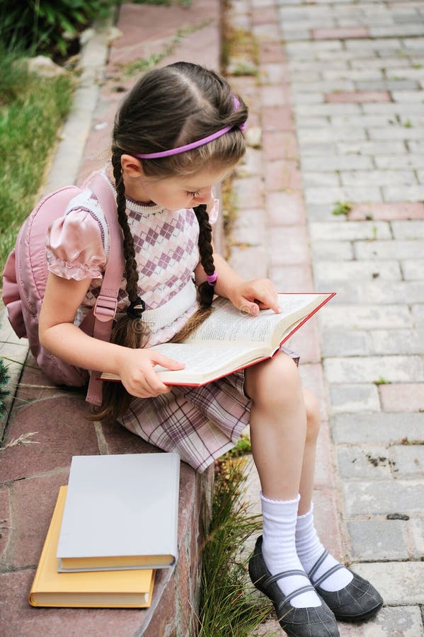 Young girl with bagpack reads waiting for school