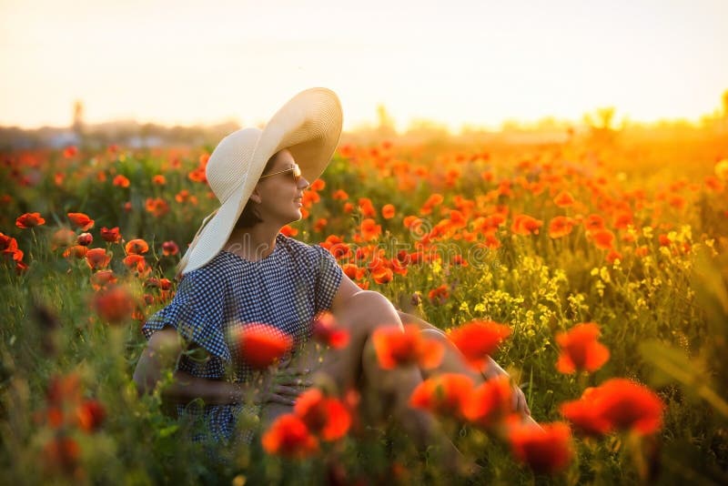 Young girl in a big hat sitting on a poppy field in sunset stock photography Young girl in a big hat sitting on a poppy field in sunset stock photography