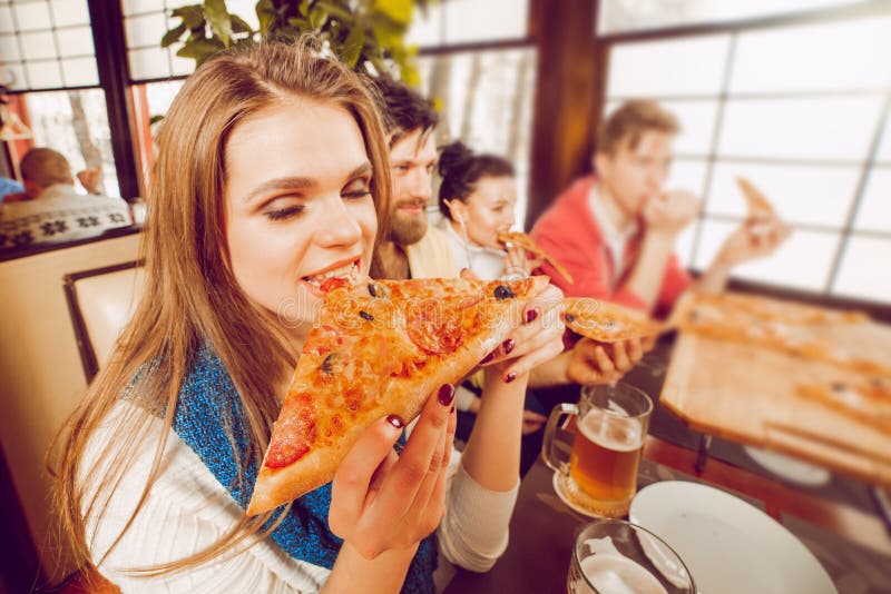 A Young Girl Bites a Large Piece of Pizza Squinting Her Eyes in ...