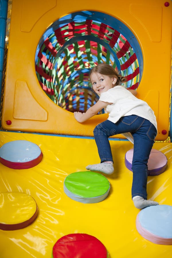 Young girl climbing up ramp into tunnel at soft play centre