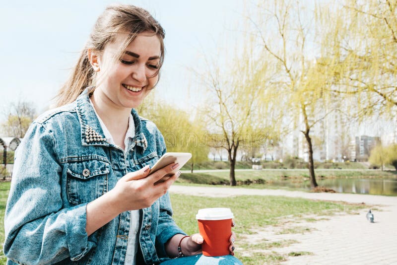 A young girl in a denim jacket walks down the street with coffee and a phone in her hands. Girl in glasses and a denim jacket on stock photo A young girl in a denim jacket walks down the street with coffee and a phone in her hands. Girl in glasses and a denim jacket on stock photo