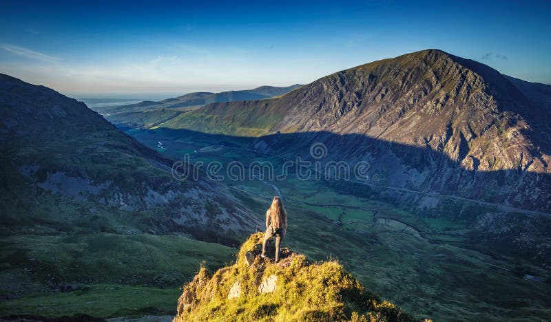 Female hiker on the edge of cliff admiring view of ice age mountains in Snowdonia North Wales, United Kingdom. Female hiker on the edge of cliff admiring view of ice age mountains in Snowdonia North Wales, United Kingdom