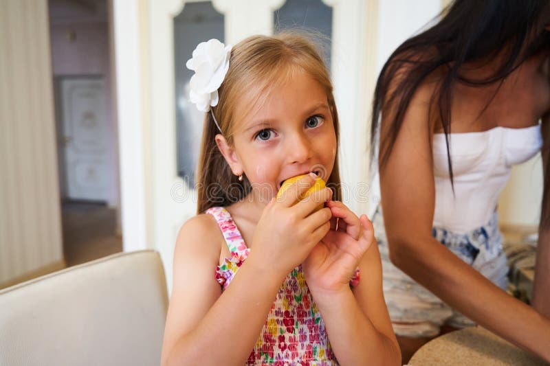 Young Girl Enjoying a Fresh Fruit Snack while Adults Prepare Food in a