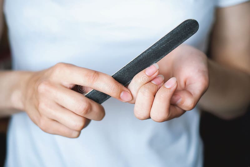 A young girl files her nails with a black nail file close-up. Women`s nails and nail file. Self-manicure at home for yourself. A w