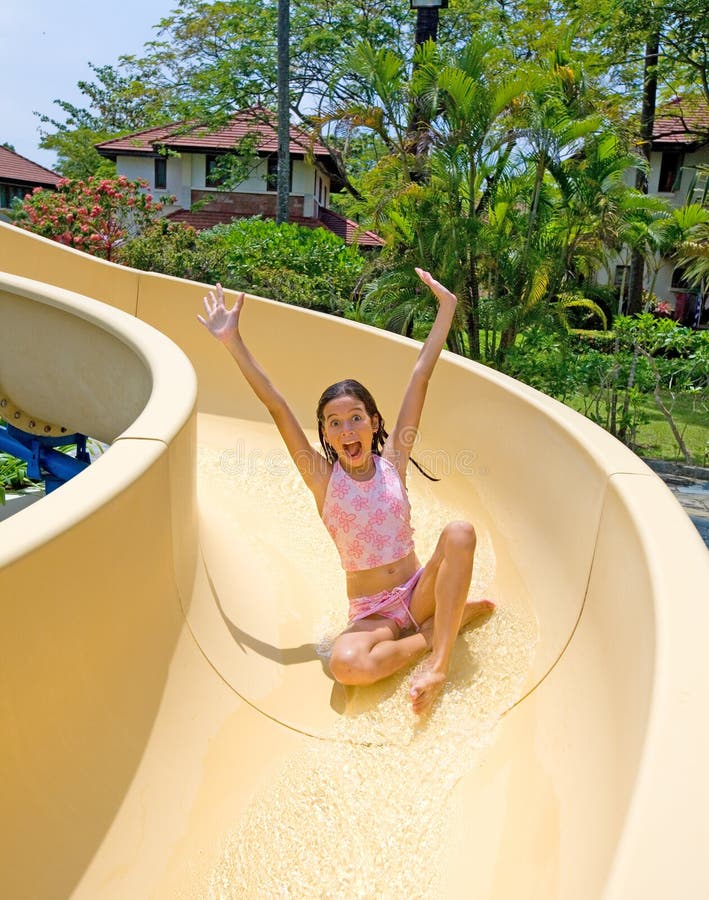 Excited young girl going down the slide at swimming pool