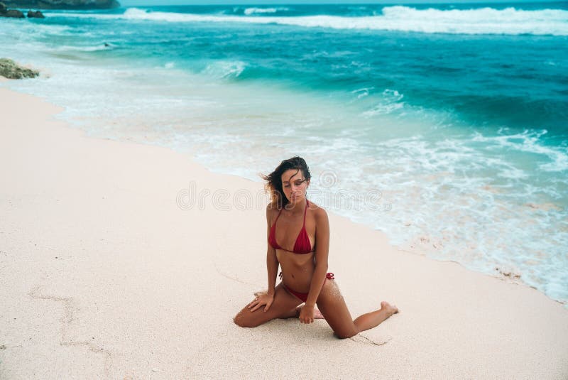 Young girl with a gorgeous body is resting on the beach with white sand near the ocean. Beautiful model in a red