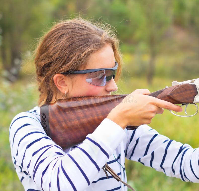 A young girl with a gun for trap shooting and shooting glasses aiming at a target