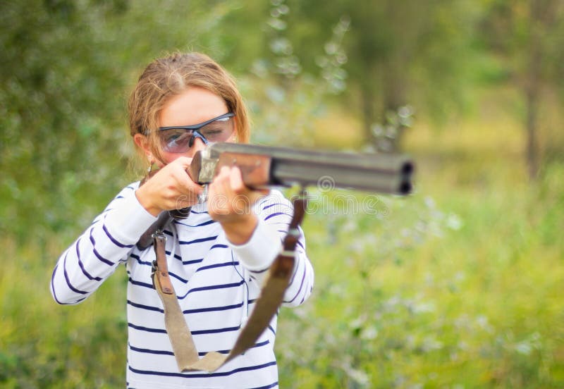 A young girl with a gun for trap shooting and shooting glasses aiming at a target. Short depth of field, focus on the face