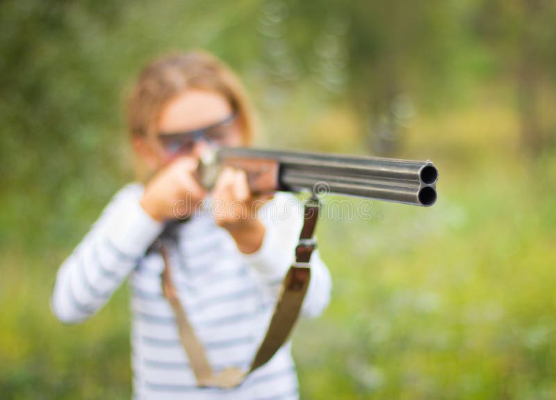 A young girl with a gun for trap shooting and shooting glasses aiming at a target. Short depth of field, focus on the barrel