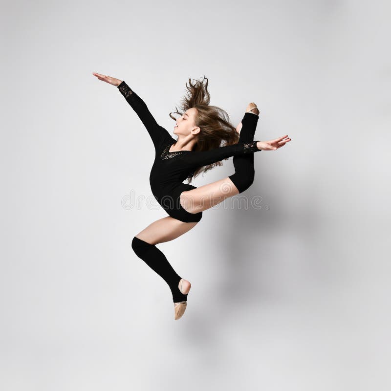 Young girl gymnast in black sport body and uppers jumping and making dymnastic pose in air over white background