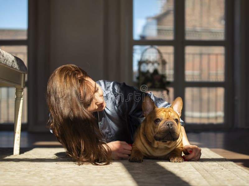 Young girl and her dog french bulldog are playing on the floor of their apartment