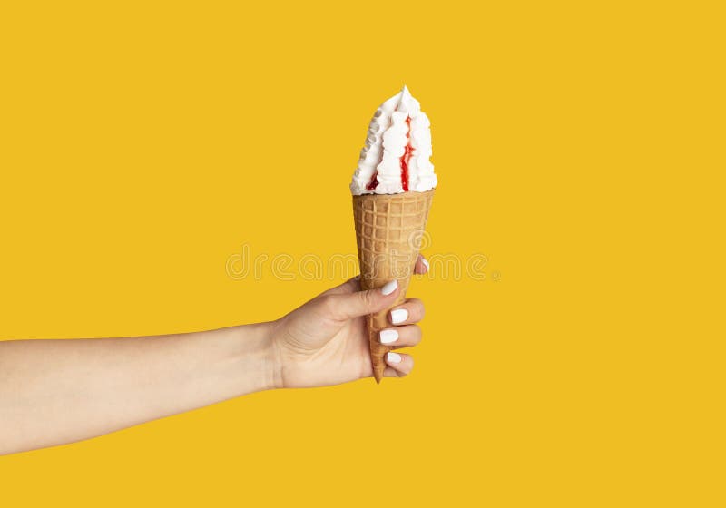 Young girl holding yummy ice cream with berry topping in waffle cone on orange background, close up of hand