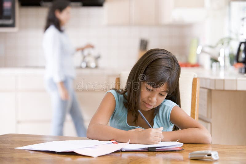 Close up of young girl in kitchen doing homework with woman in background. Standing file folder stock images, royalty-free photos and pictures