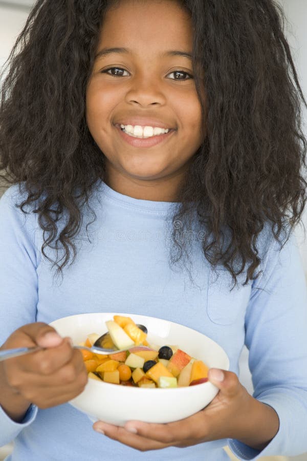 Young girl in kitchen eating bowl of fruit smiling