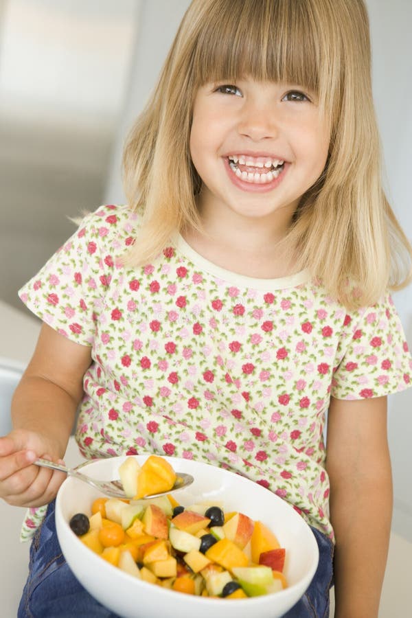 Young girl in kitchen eating bowl of fruit smiling