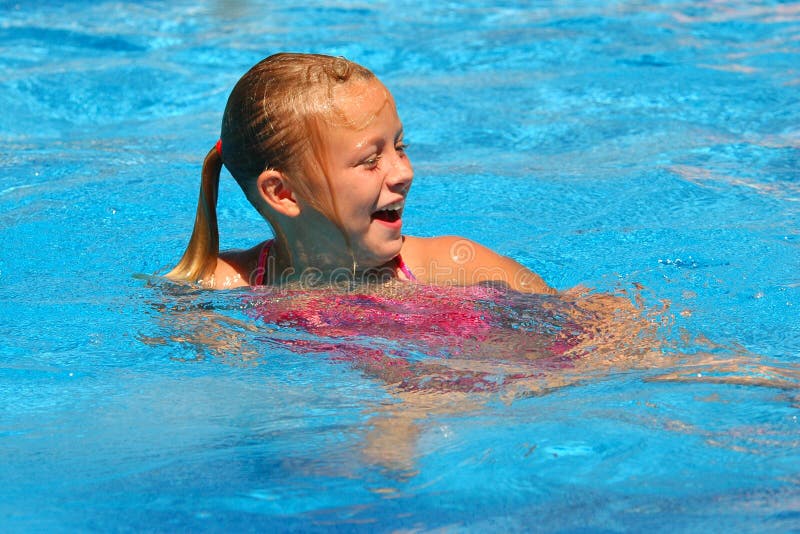 Young blond girl with pony tail laughs in a brilliant blue swimming pool. Young blond girl with pony tail laughs in a brilliant blue swimming pool