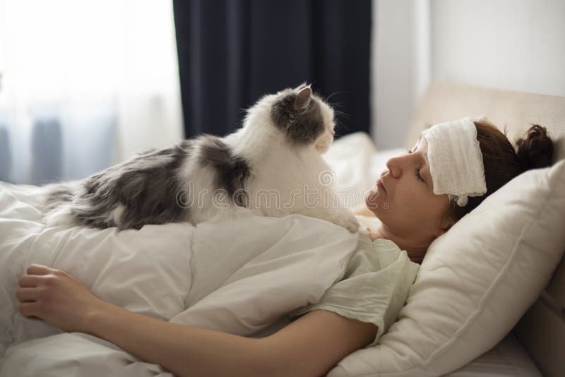 Young girl lies in bed with a fever fluffy cat treats her. Coronovirus patient