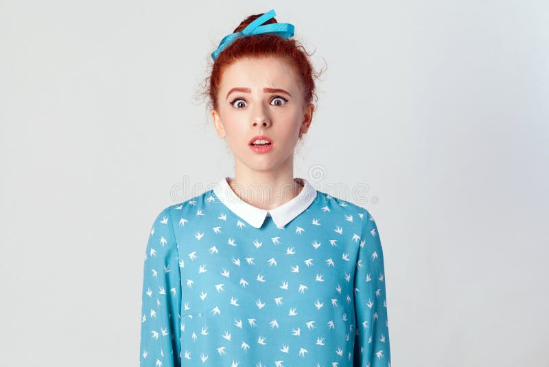 Portrait of stunned redhead young girl looking at the camera with shocked expression, mouth wide open, surprised with unexpected news. Isolated studio shot on gray background.