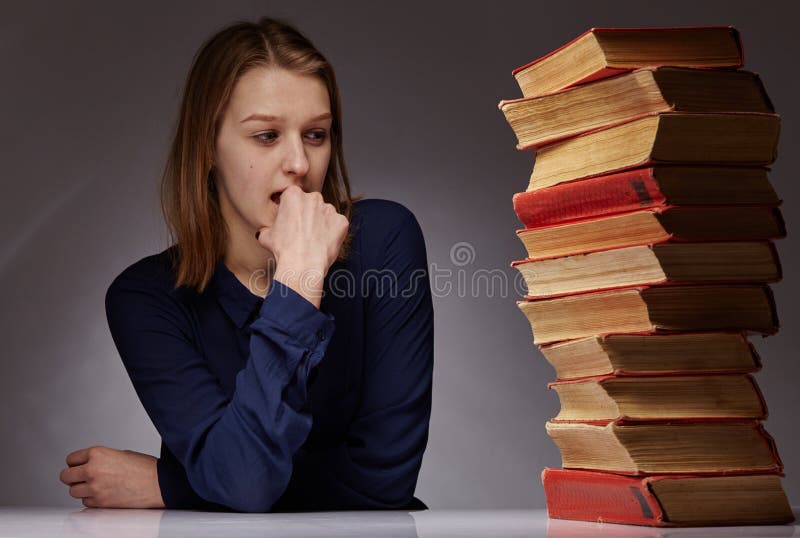 A young girl and a lot of books next to her. she has a hard time learning stock photos