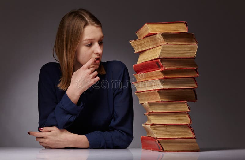 Young girl and a lot of books next to her. she has a hard time learning. stock image