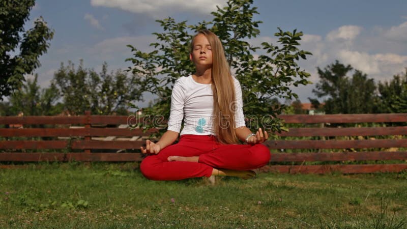 Young girl meditate in lotus position - hovering above the grass, camera slide