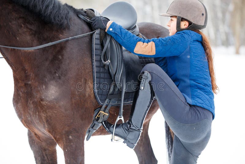 Young girl mounting on her bay horse for riding