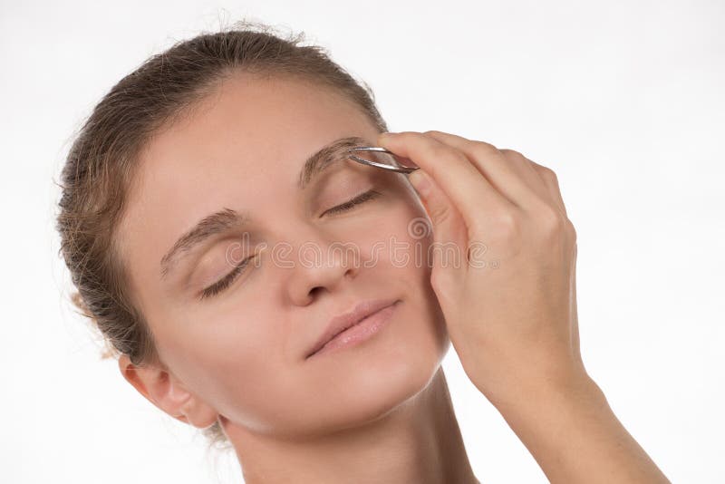 Young girl pulls out her eyebrows with tweezers metal on a white stock photography Young girl pulls out her eyebrows with tweezers metal on a white stock photography