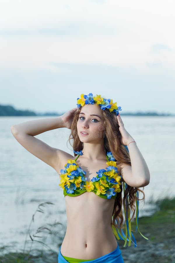 Young girl at river bank touching Ukrainian wreath with ribbons on her head. National flag colored swimsuit with flowers. Vertical shot, copy space royalty free stock images Young girl at river bank touching Ukrainian wreath with ribbons on her head. National flag colored swimsuit with flowers. Vertical shot, copy space royalty free stock images