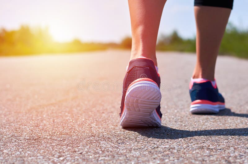 Young girl in running shoes runs along road, only her legs are visible, legs and sneakers, sunlight.