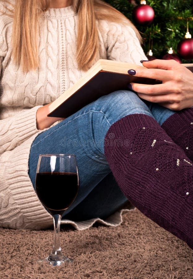 Young girl sitting on floor and reading book next to Christmas tree and coffee cup stock photo Young girl sitting on floor and reading book next to Christmas tree and coffee cup stock photo