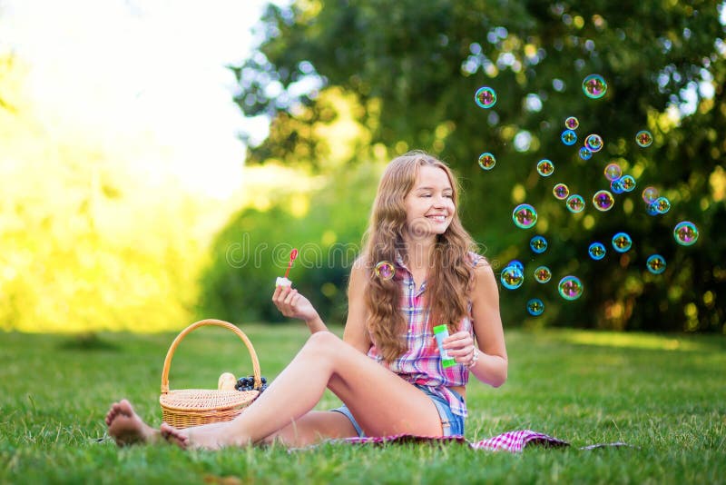 Young girl sitting on the grass blowing bubbles