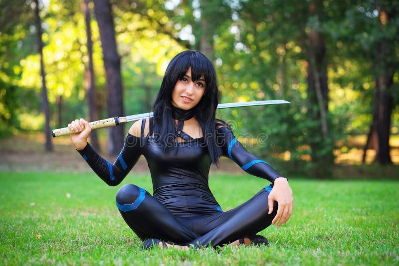 Young girl sitting on the grass and holding samurai sword.
