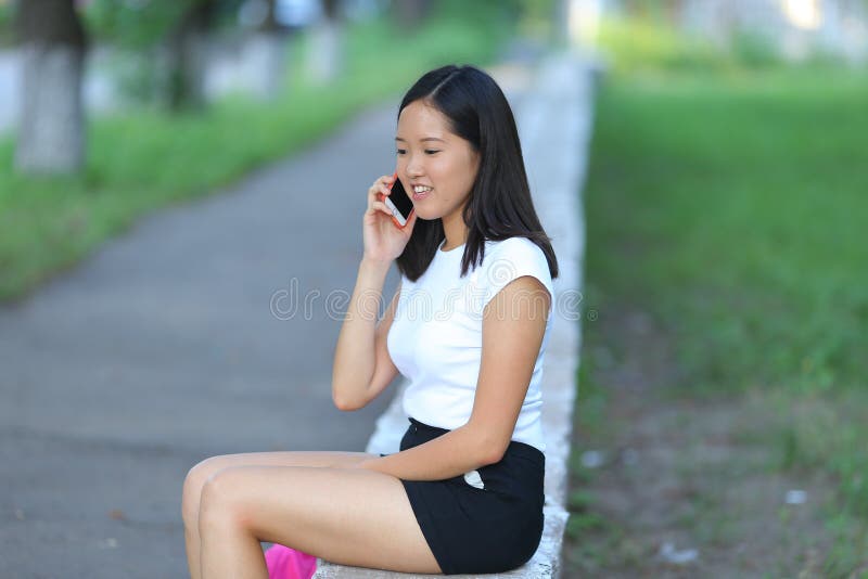 Young girl sitting and talking on the phone in the park