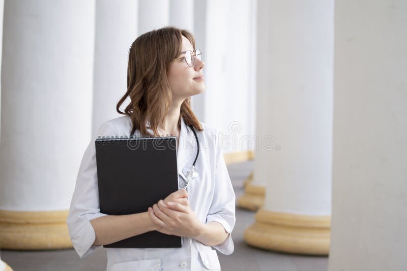 Young girl student at a medical university standing in the corridor, portrait of an attractive nurse near the hospital, happy