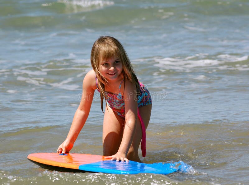 Young girl swimming in the beautiful clear blue ocean with waves crashing around her legs, and the sun shining down on her making it a picture perfect day alround.