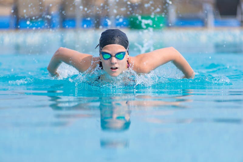 Young girl in goggles and cap swimming butterfly stroke style in the blue water pool. Young girl in goggles and cap swimming butterfly stroke style in the blue water pool