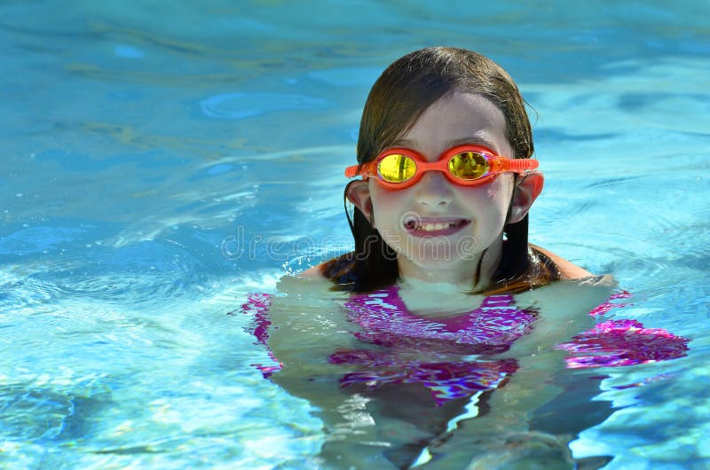 Portrait of young girl swimming with orange swim goggles in pool. Portrait of young girl swimming with orange swim goggles in pool