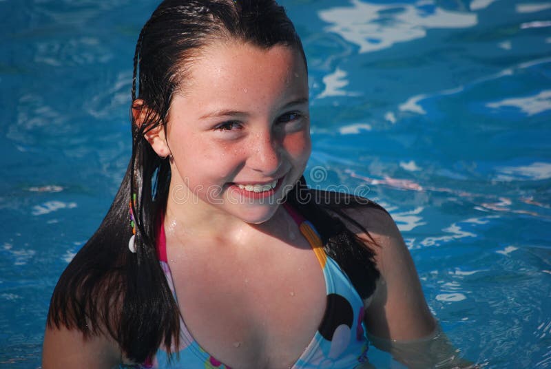 A happy smiling brown-eyed brown haired preteen girl swimming in a pool on a sunny day. A happy smiling brown-eyed brown haired preteen girl swimming in a pool on a sunny day.