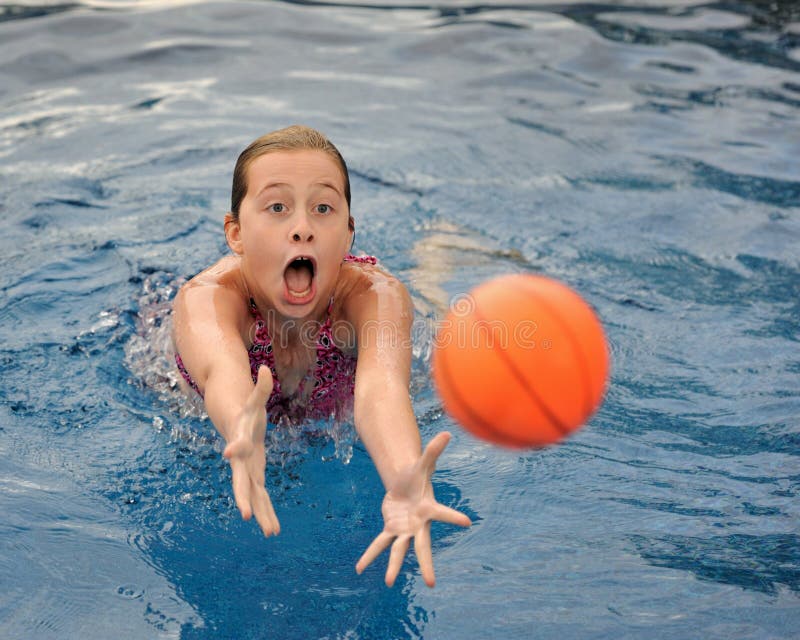 Young brunette caucasian girl diving for orange ball in swimming pool. Young brunette caucasian girl diving for orange ball in swimming pool