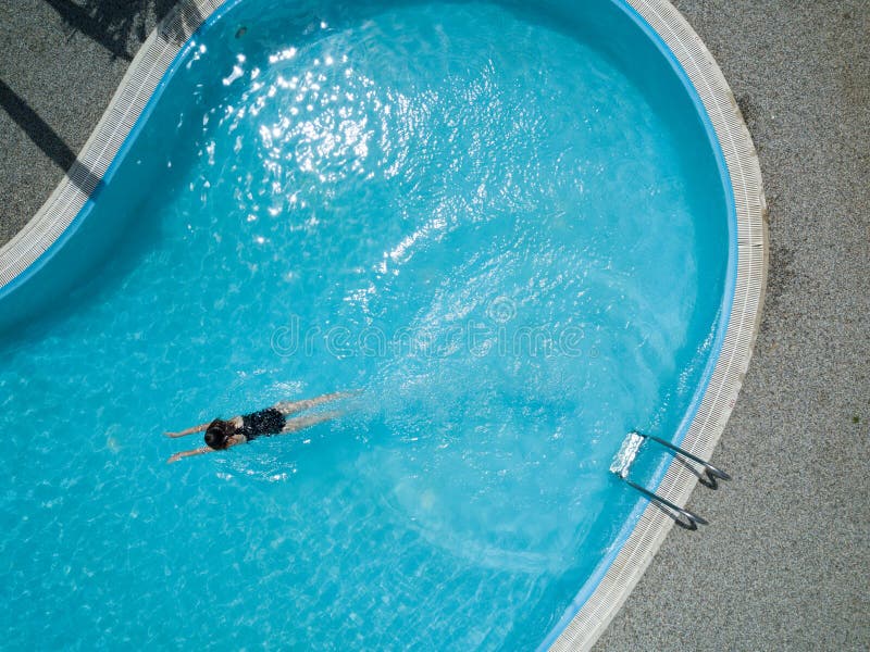 Young girl swims in blue swimming pool, from up. Aerial image, drone picture.