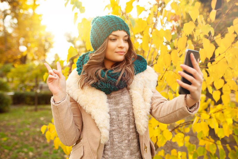 Young girl takes a selfie on the backgroung autumn beautiful leaves. Autumn concept. Videobloger