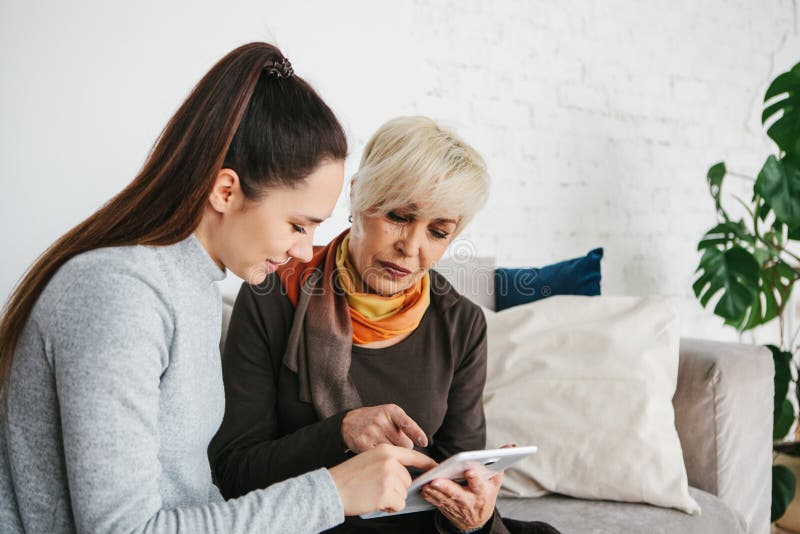 A young girl explains to an elderly woman how to use a tablet or shows some application or teaches you how to use a stock image A young girl explains to an elderly woman how to use a tablet or shows some application or teaches you how to use a stock image