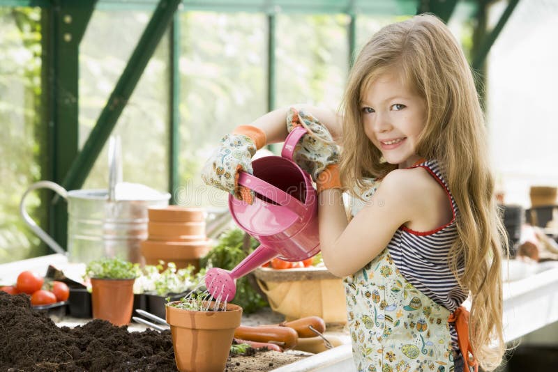 Mladá dívka zalévání rostlin ve skleníku s úsměvem.